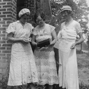 Having baked rolls three women pose outside with pans and other kitchen utensils