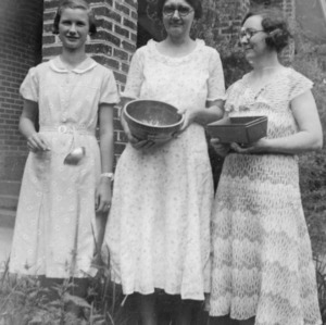 Three women posing outside with pans and other kitchen utensils