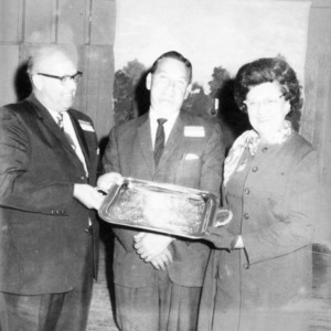Two men and one woman holding a decorative platter