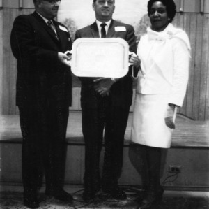 Two men and one woman holding a platter in front of a stage