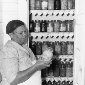 Woman standing in front of a pantry holding a jar of preserves