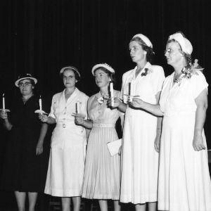 Women on stage singing and holding candles