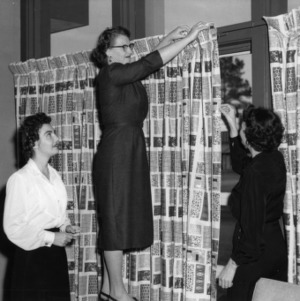 Three women hanging curtains from sewing project
