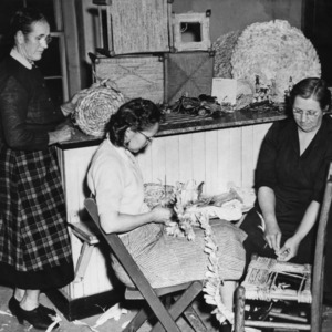 Three women reweaving the seat of a chair