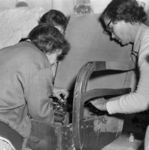Three women working on the springs in the seat of a chair
