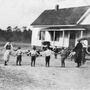 Group of children and two adults standing outside, holding hands in a circle