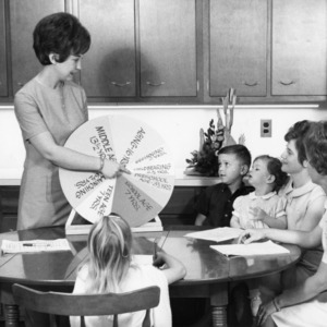 Home economics extension worker talking to mothers and children sitting at kitchen table, May 25, 1967