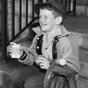 Young boy holding a bat, ball, glove, and a carton of milk