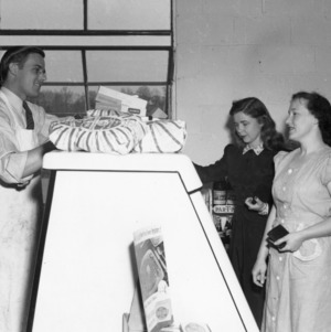 Two women being waited on by the butcher in the Vetville Mutual Grocery Co-op.