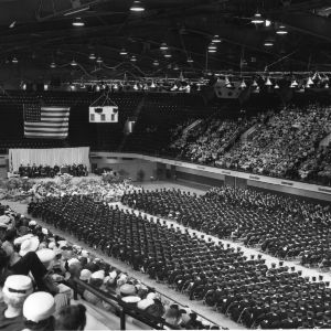 View of stage, graduates, and audience at North Carolina State College commencement ceremony in Reynolds Coliseum.