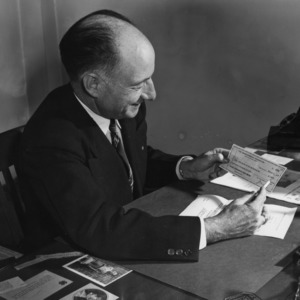 L. R. Harrill sitting at his desk holding a check from the Sears-Roebuck Foundation for $7,500