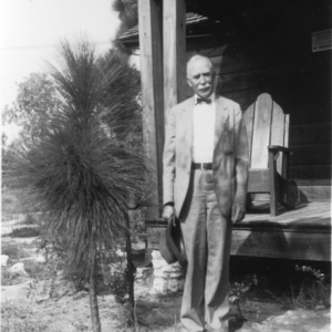 Man in suit standing outside house with sapling