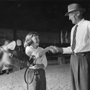 4-H club member Jane Stokes holding her calf and shaking hands with an unidentified man
