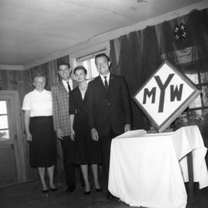 State 4-H young men and women officers standing next to the YMW sign