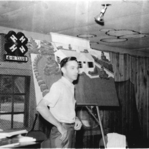 Unidentified man standing in front of the 4-H symbol attending the Young Men and Women's Conference in Manteo, North Carolina