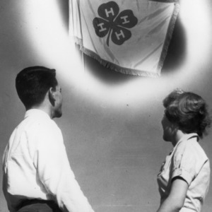 Two 4-H club members holding hands and looking up at a 4-H flag
