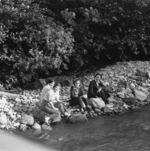 Four women sitting on bank of river at John's River Camp, 1938