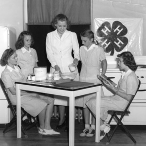 Four 4-H club girls watching a food preparation demonstration by a 4-H leader