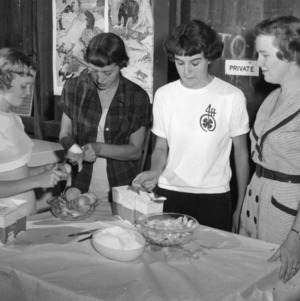 Three 4-H club girls preparing food under the supervision of a 4-H home agent