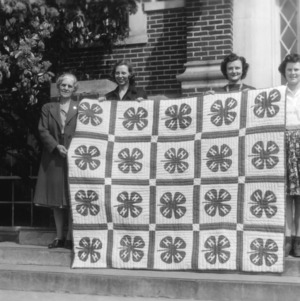 Three 4-H club girls and their leader holding a 4-H club quilt