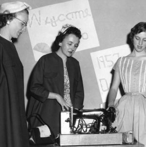 Three 4-H club winners in the home economics program examining a sewing machine