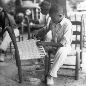 African-American boy weaves seat caning onto a chair, Guilford County, North Carolina, September 1937
