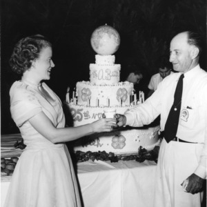L. R. Harrill handing a drink to an unidentified woman in front of a 25th anniversary of 4-H cake