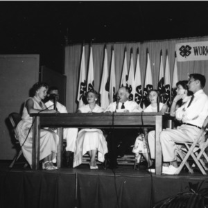 4-H club leaders, with L. R. Harrill, North Carolina State 4-H Club leader, center, sitting onstage at table and speaking into microphones