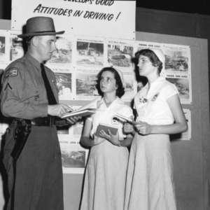 Two 4-H club members standing with a highway patrolman at a 4-H demonstration during North Carolina State 4-H Club Week