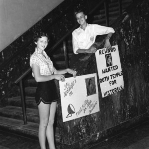 Young woman holding sign reading "The spotlight's on Neal Kelly for State Vice-President," and young man holding sign reading "Reward, Wanted, Ruth Temple for Historian," during North Carolina State 4-H Club Week