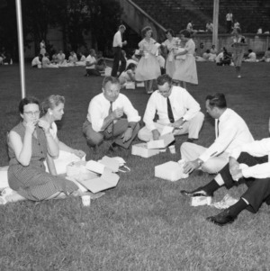 L. R. Harrill, North Carolina State 4-H Club leader, and others eating box lunches on football field, during North Carolina State 4-H Club Week