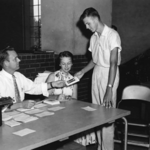 Young man receiving information from a seated man and woman, during North Carolina State 4-H Club Week