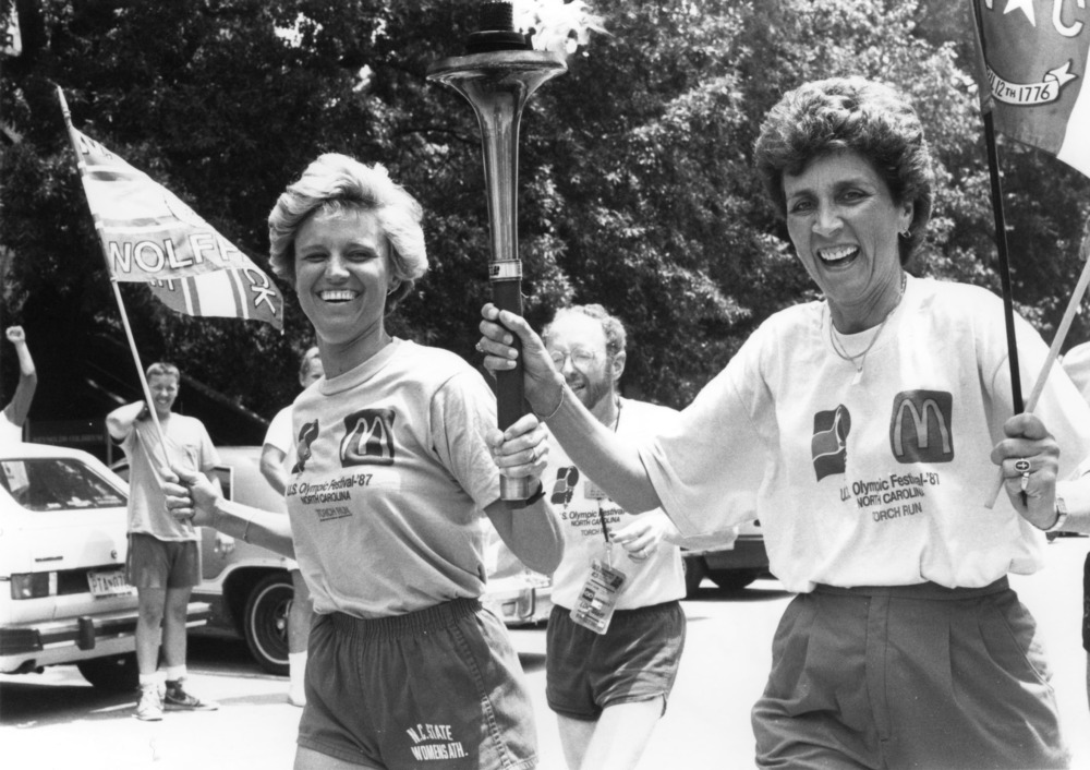 Black and white photo of two women running and carrying a torch and flags