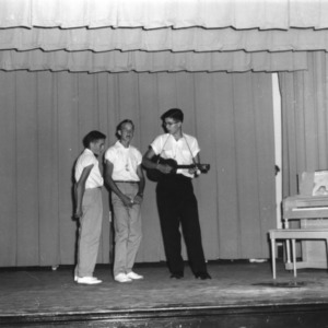 One 4-H club boy playing guitar while two others sing at a North Carolina State 4-H Club Week performance