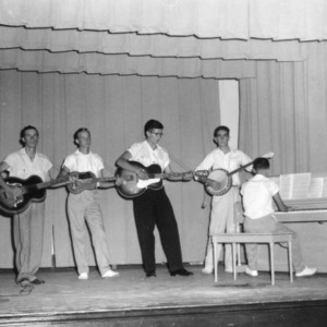 Five 4-H club boys playing in a string band, including piano, at a North Carolina State 4-H Club Week performance