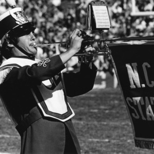 Wolfpack marching band member playing horn with N.C. State banner
