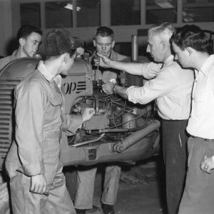 4-H instructor Ferguson adjusting the valves on a tractor at a 4-H tractor program in front of, left to right, Justice Ammons of Madison County, Allen Bleims of Allegheny County, Junior Parrish of Swain County and Larry Best of Iredell County