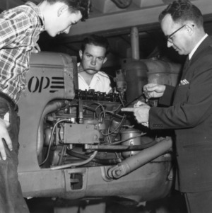 Howard Todd, Director of Youth Activities of American Oil Company shows Ral[ch?] Walker of Burke [County] (left) and Larry Best of Iredell [County] how to check oil in a tractor