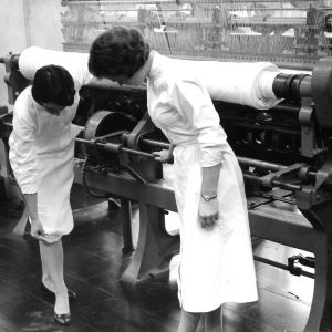 Two women working in a textile factory with a knitting machine