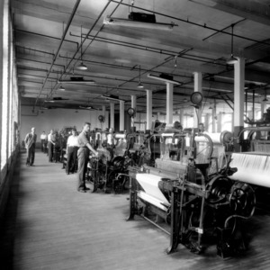 Dean Thomas Nelson standing on left in textile machine room in Tompkins Hall