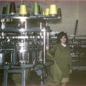 Woman posing with the machine she used to make the coat she is wearing