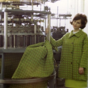 Woman posing with the machine she used to make the coat she is wearing