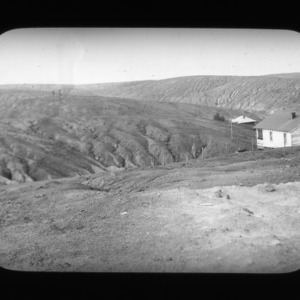 Bare gullies on hillside with two houses