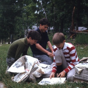 Three boys leaf through a bundle of newspapers