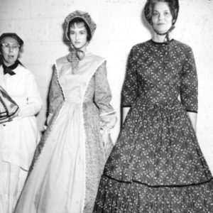Three women wearing 19th century dresses