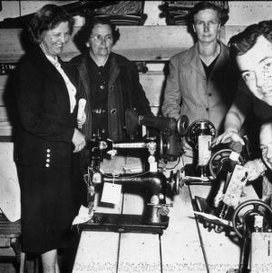 Men and women standing around a table with sewing machines