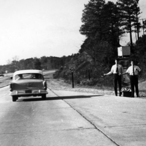 Two men trying to catch a ride on the side of the road
