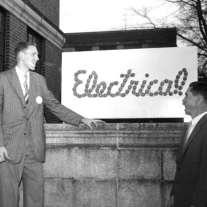 Men examining "Electrical" sign outside building