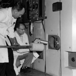 Laboratory Technician Harold Carter and Dr. Wesly Doggett loading a sample into the reactor for irradiation