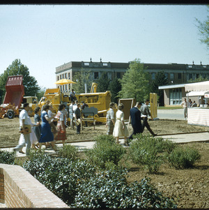 People walking past farm equipment, circa April 1959